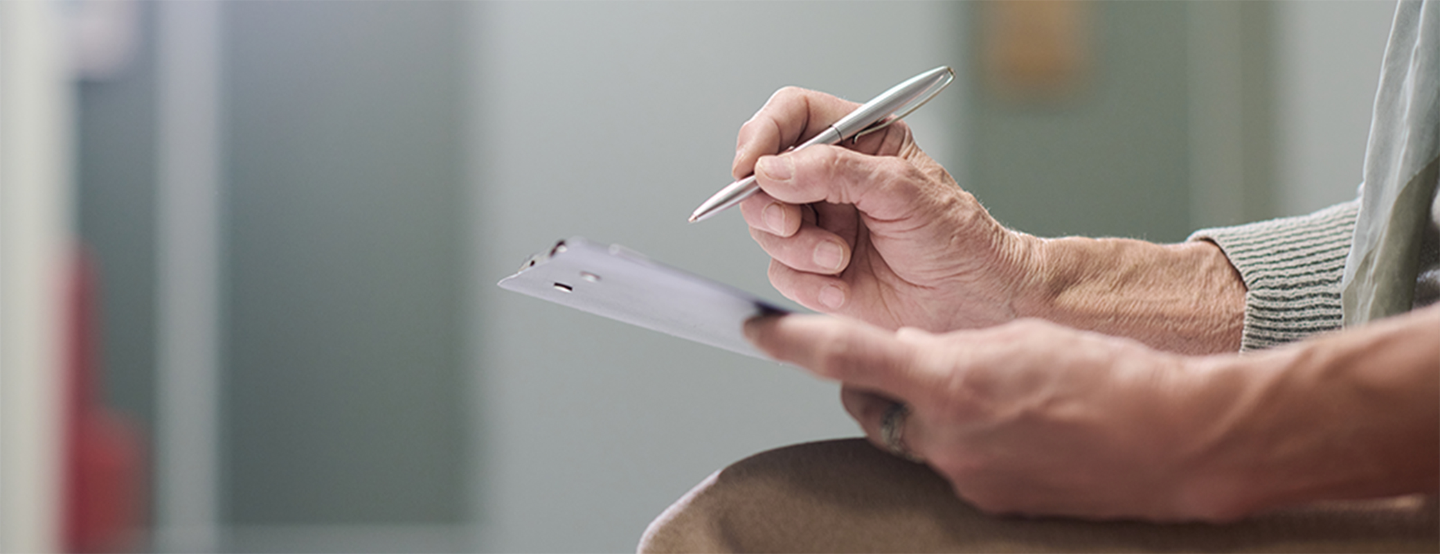 Image of senior hands filling out paperwork on a clipboard